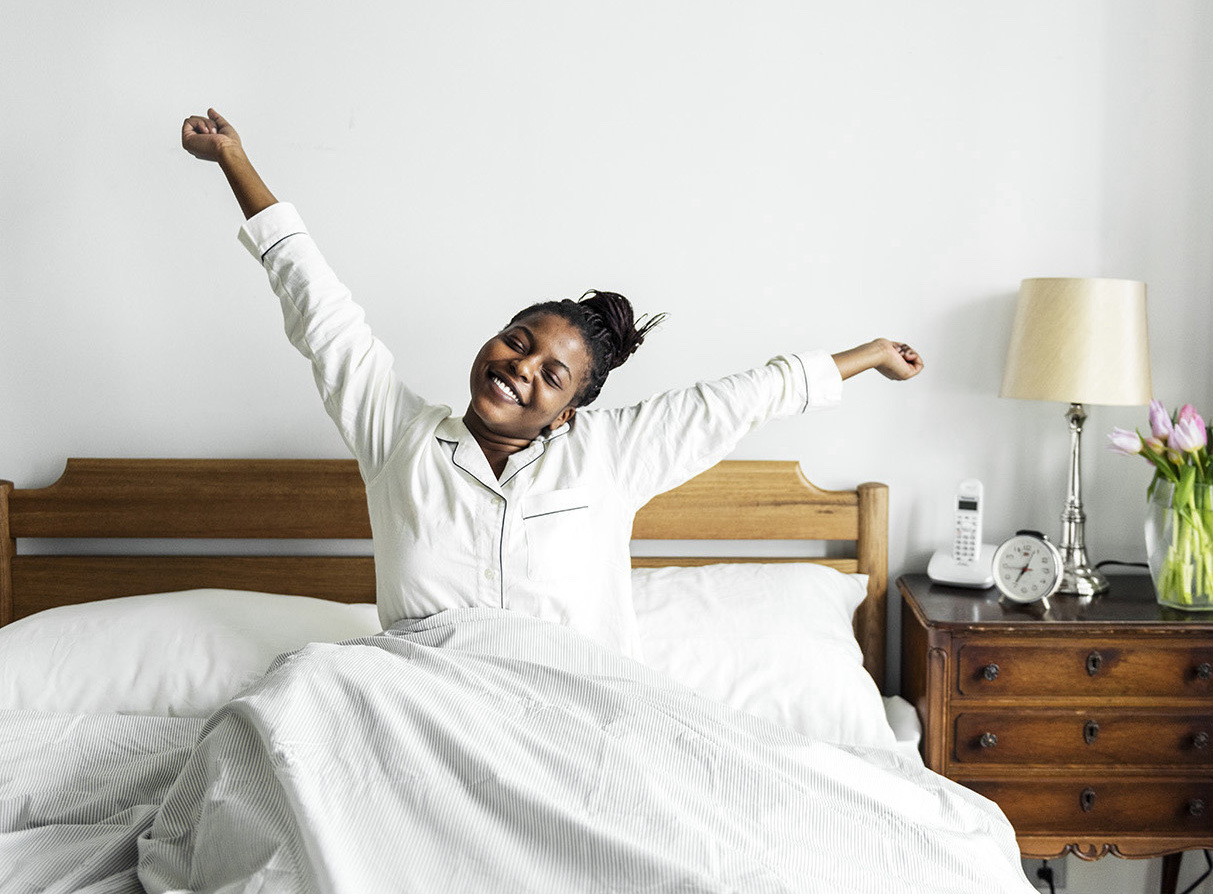 A woman smiling and stretching in bed, feeling refreshed after a good night's sleep, representing the benefits of overcoming insomnia.